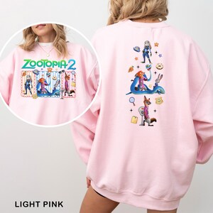 May include: Light pink sweatshirt featuring the text "ZOOTOPIA 2" on the front, with cartoon characters. The back of the sweatshirt has a colorful graphic of characters and elements from the movie. The sweatshirt is made of a soft material.