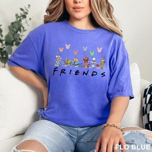 May include: A blue t-shirt featuring a graphic of cartoon characters holding balloons, with the word "FRIENDS" in a colorful font. The shirt is a solid blue color.