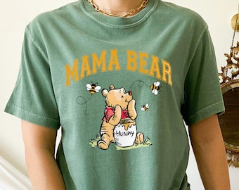 May include: Green t-shirt with a cartoon Winnie the Pooh bear holding a pot of honey. The text "Mama Bear" is printed in yellow above the bear.