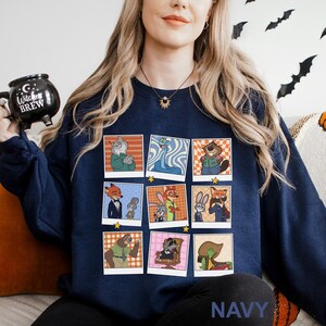 May include: Navy blue sweatshirt featuring a grid of cartoon character portraits in a polaroid style. The characters are anthropomorphic animals. The word "NAVY" is printed at the bottom. A black mug with the words "Witches Brew" is held in the upper left.