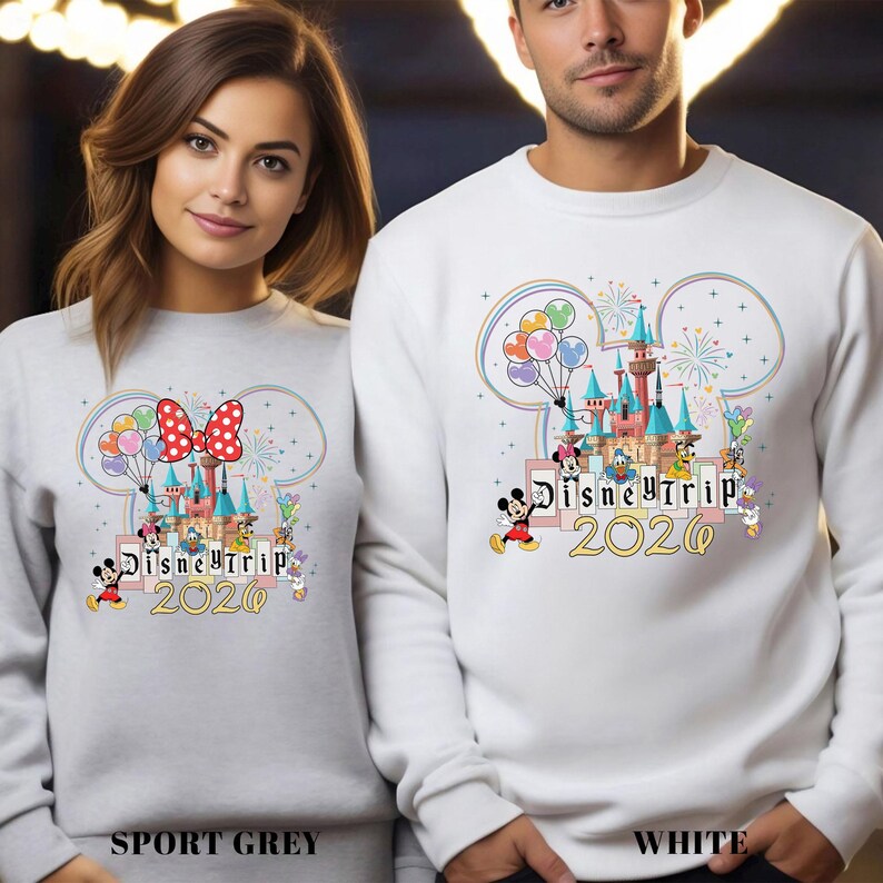 Puede incluir: Sudaderas grises deportivas y blancas con un dise&ntilde;o de Disney Trip 2020. El dise&ntilde;o presenta un castillo, Mickey Mouse, Minnie Mouse y otros personajes, con globos y fuegos artificiales. Las sudaderas tienen cuello redondo.