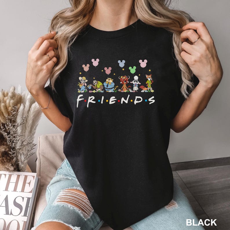 May include: Black crew neck t-shirt featuring a colorful graphic of cartoon characters and the word "FRIENDS" in a rainbow font. Above the characters are Mickey Mouse head shapes in various colors. The word "BLACK" is in the bottom right corner.