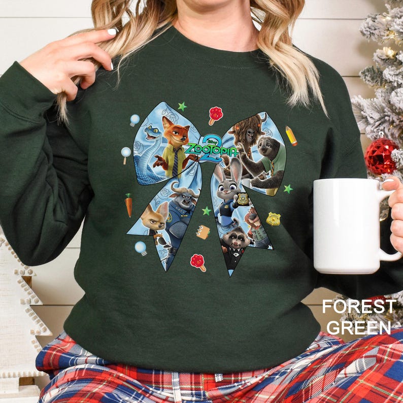 May include: Forest green sweatshirt featuring a large bow design with characters from the animated film "Zootopia." The bow includes images of a fox, a bunny, and other animal characters. The text "Zootopia" is in the center of the bow.