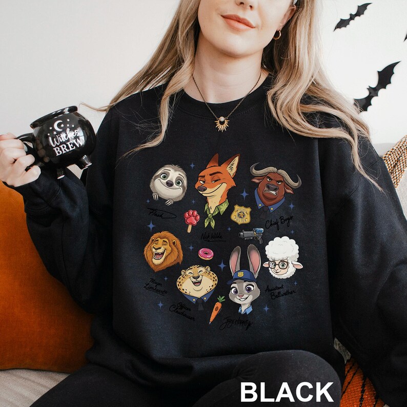 K&ouml;nnte beinhalten: Schwarzes Sweatshirt mit Illustrationen von Zeichentrickfiguren. Das Design umfasst ein Faultier, einen Fuchs, einen L&ouml;wen, einen Geparden, ein Kaninchen und andere Charaktere. Das Wort "BLACK" ist unten auf dem Sweatshirt aufgedruckt.
