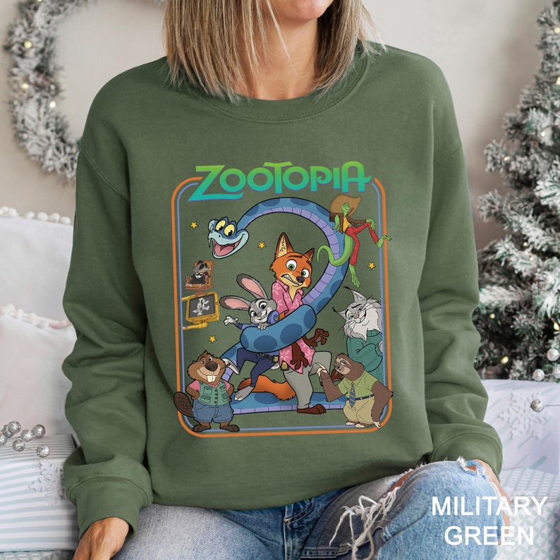 May include: Military green sweatshirt featuring a colorful graphic from the animated film "Zootopia." The design includes the film's title and various characters, such as a fox, rabbit, and sloth. The sweatshirt is a crew neck style.