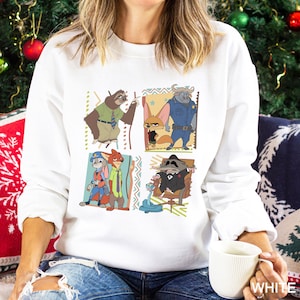 May include: White sweatshirt featuring cartoon characters from Zootopia. The design includes images of Flash, Nick Wilde, Judy Hopps, Chief Bogo, Finnick, and Mr. Big. The sweatshirt has a crew neck and long sleeves. The word "WHITE" is printed on the bottom right.