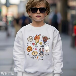 K&ouml;nnte beinhalten: Wei&szlig;es Sweatshirt mit Zeichentrickfiguren aus dem Film Zoomania. Das Design umfasst Bilder von Flash, Nick Wilde, Chief Bogo, Judy Hopps und anderen. Das Wort "WHITE" ist unten aufgedruckt.