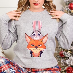 May include: A light gray sweatshirt featuring a cartoon image of a fox and a rabbit. The fox is orange with a sly expression, and the rabbit is gray with long pink ears. The text "Sport Grey" is at the bottom.