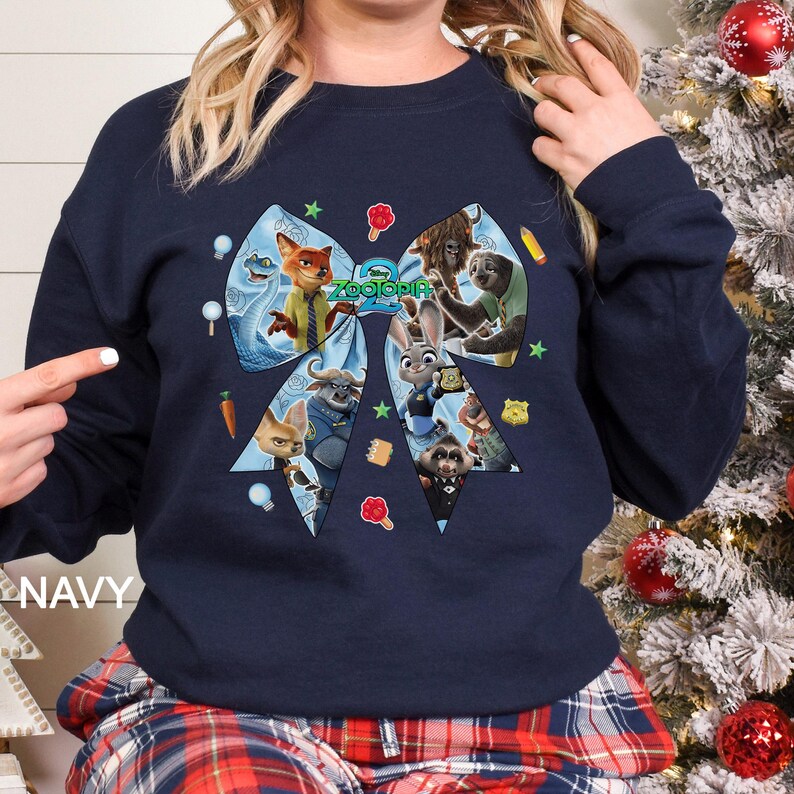 May include: Navy blue sweatshirt featuring a large bow design with characters from the animated movie Zootopia. The bow is filled with images of the characters, and the word "Zootopia" is in the center. The word "NAVY" is printed on the bottom left.