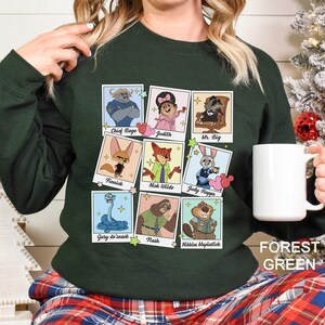 Pu&ograve; includere: Felpa verde foresta con un collage di ritratti di personaggi dei cartoni animati. I personaggi includono Chief Bogo, Judith, Mr. Big, Finnick, Nick Wilde, Judy Hopps, Gary de'snack, Flash e Nibbles Maplestick. Il testo "FOREST GREEN" &egrave; stampato in basso a destra.