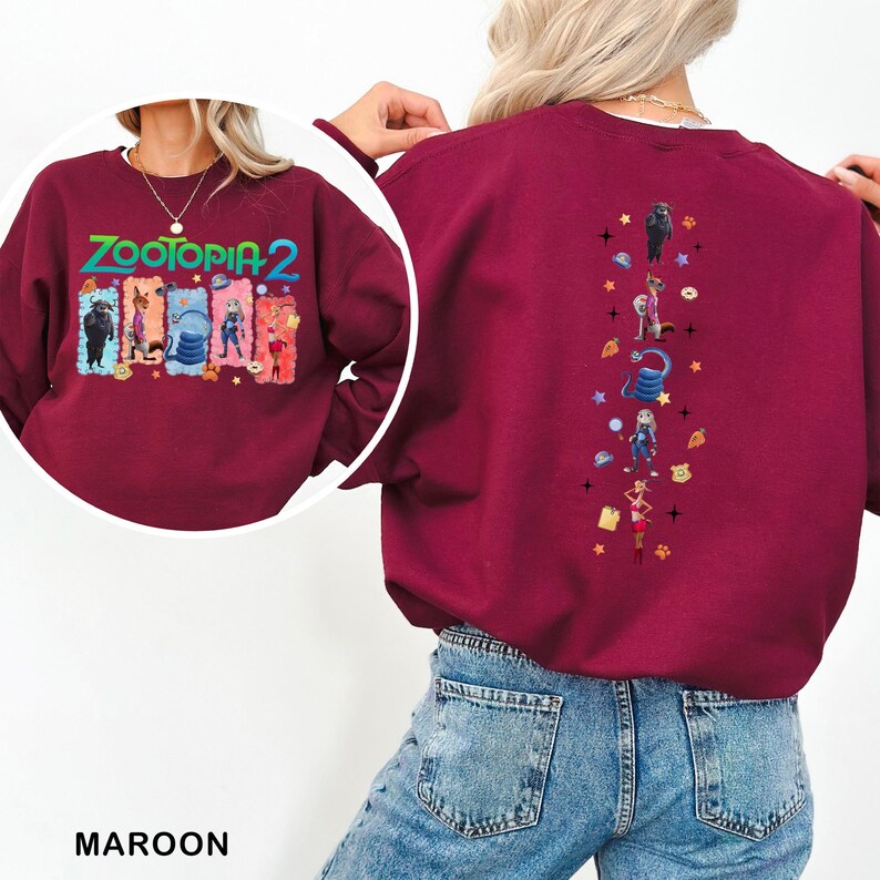 K&ouml;nnte beinhalten: Burgunderfarbenes Sweatshirt mit dem Text "ZOOTOPIA 2" in Gr&uuml;n, Orange und Blau. Die Grafik auf der Vorderseite zeigt Charaktere aus dem Film. Die R&uuml;ckseite des Sweatshirts hat ein vertikales Design mit weiteren Charakteren und Sternen.