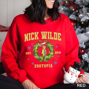 Pu&ograve; includere: Una felpa rossa con la scritta "NICK WILDE" in verde, con un personaggio dei cartoni animati a forma di volpe con un cappello di Babbo Natale e un design a ghirlanda. La felpa include anche il testo "EST. 2016 ZOOTOPIA".
