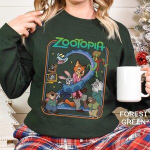 May include: Forest green sweatshirt featuring a colorful graphic from the movie Zootopia. The design includes characters like Judy Hopps, Nick Wilde, and others, with the word "Zootopia" at the top. The sweatshirt is a crew neck style.