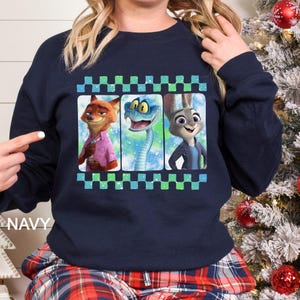 May include: Navy blue sweatshirt featuring a graphic of three animated characters: a fox, a snake, and a rabbit. The design is framed with a green and blue checkered border. The word "NAVY" is printed on the bottom left.