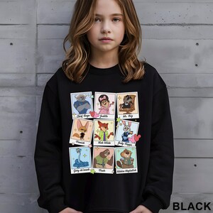 Pu&ograve; includere: Felpa nera con una griglia di ritratti di personaggi dei cartoni animati, tra cui Chief Bogo, Judy e Nick Wilde. La parola "BLACK" &egrave; stampata in basso sulla felpa.