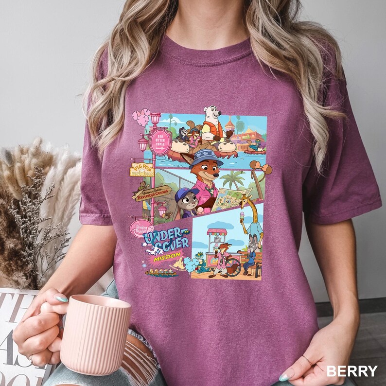 May include: A berry-colored short-sleeve t-shirt featuring a graphic print of Zootopia characters in various scenes. The design includes the text Undercover Mission and depicts a fox and rabbit exploring a park, riding a boat, and eating ice cream.