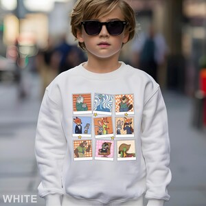 May include: White sweatshirt featuring a grid of cartoon character images. The images are in a polaroid style with a star at the bottom. The word "WHITE" is printed at the bottom left of the sweatshirt.