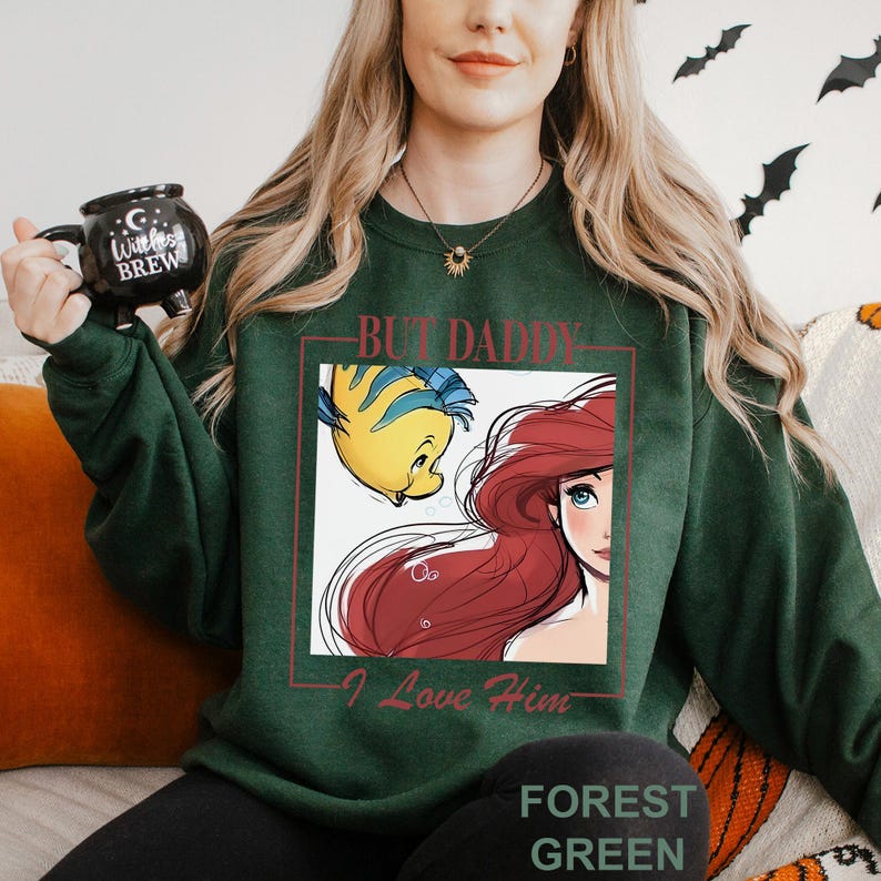 May include: Forest green sweatshirt with a graphic of Ariel and Flounder from The Little Mermaid, and the text "But Daddy, I Love Him." The sweatshirt has a crew neck and is a solid colour.