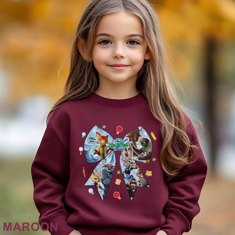 May include: A maroon sweatshirt featuring a colorful graphic of characters from the animated movie "Zootopia" in a bow shape. The word "MAROON" is printed at the bottom left of the image.
