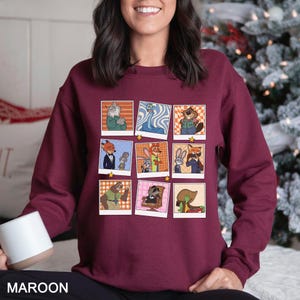 May include: Maroon sweatshirt featuring a grid of cartoon character images in polaroid-style frames. The characters are anthropomorphic animals in various outfits. The word "MAROON" is printed at the bottom of the sweatshirt.