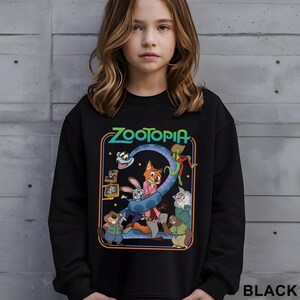 May include: Black sweatshirt featuring the word "ZOOTOPIA" in green and blue, with a cartoon graphic of characters from the movie. The graphic includes a fox, rabbit, and other animals. The word "BLACK" is printed at the bottom right.