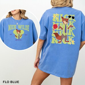Op de afbeelding: Een blauw t-shirt met een afbeelding van het personage Nick Wilde uit Zootopia. De voorkant toont de tekst Nick Wilde met een kleine illustratie. De achterkant toont een grote afbeelding van Nick Wilde met de herhaalde tekst Nick.