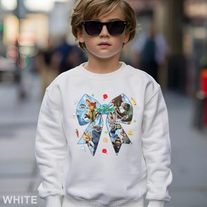 May include: White sweatshirt featuring a large, colorful graphic of characters from the movie "Zootopia" in a bow shape. The graphic includes images of a fox, a bunny, and other animals. The word "Zootopia" is also visible in the graphic.