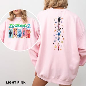 K&ouml;nnte beinhalten: Hellrosa Sweatshirt mit dem Schriftzug "ZOOTOPIA 2" und Cartoonfiguren. Auf der R&uuml;ckseite befindet sich ein vertikales Design mit Cartoonfiguren und Sternen. Der untere Teil des Bildes tr&auml;gt den Text "LIGHT PINK".