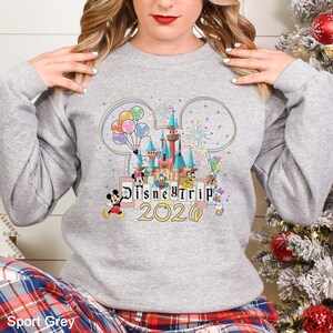Puede incluir: Sudadera gris claro con un dise&ntilde;o colorido del castillo de Disney con Mickey Mouse, Donald Duck y otros personajes. El texto "Disney Trip 2020" se muestra debajo. La sudadera es de color Sport Grey.