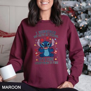 a woman sitting on a bed wearing a red sweatshirt