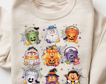 May include: Beige sweatshirt featuring a colorful Halloween-themed graphic. The graphic includes various cartoon characters such as ghosts, pumpkins, and vampires. The design is surrounded by spiderwebs, creating a festive and playful look.