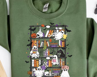 May include: Olive green sweatshirt featuring a whimsical illustration of ghosts reading books on a bookshelf, with bats, pumpkins, and a black cat. The design has a Halloween theme.