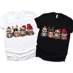 May include: Five raccoons wearing Santa hats and Christmas lights, with one wearing a top hat. The raccoons are on a white and black t-shirt.