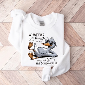 May include: White sweatshirt with a cartoon duck wearing sunglasses and the text "WHATEVER LIFE THROWS AT YOU, duck and let it HIT SOMEONE ELSE."