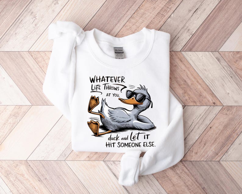 May include: White sweatshirt with a cartoon duck wearing sunglasses and the text "WHATEVER LIFE THROWS AT YOU, duck and let it HIT SOMEONE ELSE."