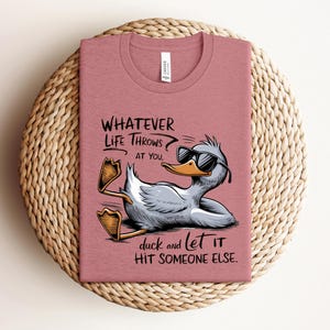 May include: A pink t-shirt with a cartoon duck wearing sunglasses and the text "WHATEVER LIFE THROWS AT YOU, duck and let IT HIT SOMEONE ELSE."