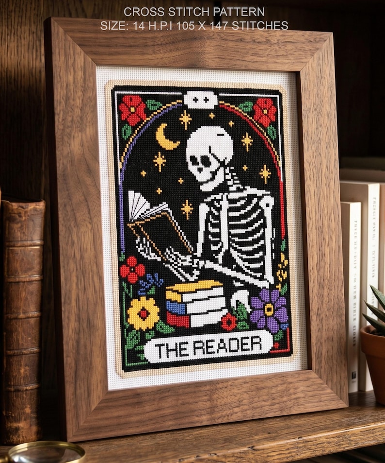 K&ouml;nnte beinhalten: Gerahmtes Kreuzstichmuster mit einem Skelett, das ein Buch liest, vor schwarzem Hintergrund mit floralen Akzenten. Der Text "THE READER" steht unten. Der Rahmen ist aus Holz. Die Gr&ouml;&szlig;e betr&auml;gt 105 x 147 Stiche.