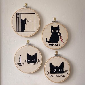 Peut inclure: Quatre tambours &agrave; broder circulaires en bois contenant des points de croix de chats noirs. L'un montre un chat qui regarde avec le texte "bitch...", un autre un chat tenant un couteau avec "WHAT?", un chat dans l'eau et "EW, PEOPLE".