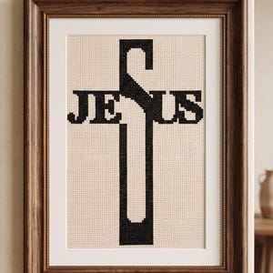 Pu&ograve; includere: Un ricamo a punto croce incorniciato che presenta la parola JESUS in filo nero su uno sfondo di tessuto color crema. La lettera J forma la parte superiore della croce, mentre la lettera S forma la barra orizzontale. L'opera &egrave; in una cornice di legno scuro.