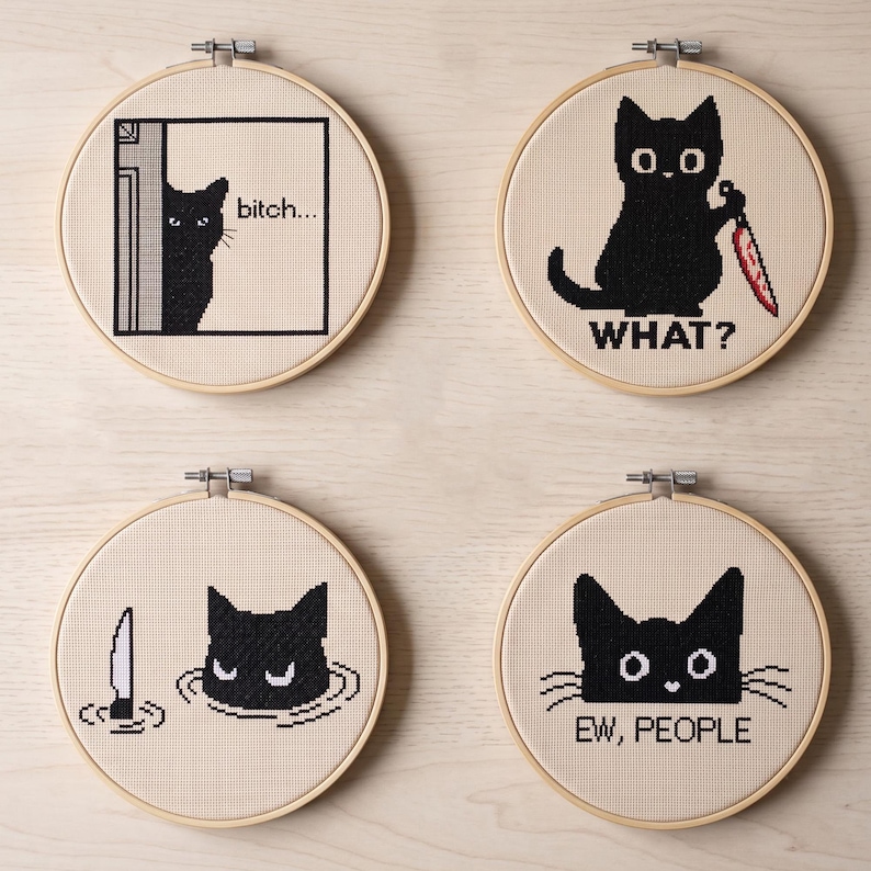 Peut inclure: Quatre tambours &agrave; broder circulaires en bois contenant des points de croix sur tissu beige. Les motifs montrent des chats noirs avec du texte : un qui regarde en disant "bitch...", un tenant un couteau ensanglant&eacute; "WHAT?", un dans l'eau et "EW, PEOPLE".