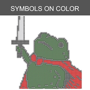 May include: A cross-stitch pattern titled SYMBOLS ON COLOR featuring a pixelated green frog character wearing a red cape and holding a sword aloft. The design uses a grid of small heart and clover symbols to represent colours in a blocky style.