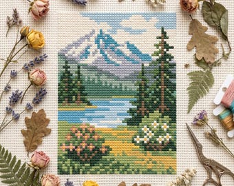 Peut inclure: Une broderie au point de croix représentant un paysage de montagne, un lac et des arbres à feuilles persistantes. La scène est réalisée dans des tons de bleu, vert et jaune. Des fleurs séchées, des feuilles et du matériel de broderie entourent l'œuvre encadrée.