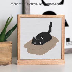 Peut inclure: Un motif de point de croix encadr&eacute; repr&eacute;sentant un chat noir dans une bo&icirc;te en carton. Le chat a des moustaches blanches. Le texte "CROSS STITCH PATTERN - INSTANT DOWNLOAD" est en haut.