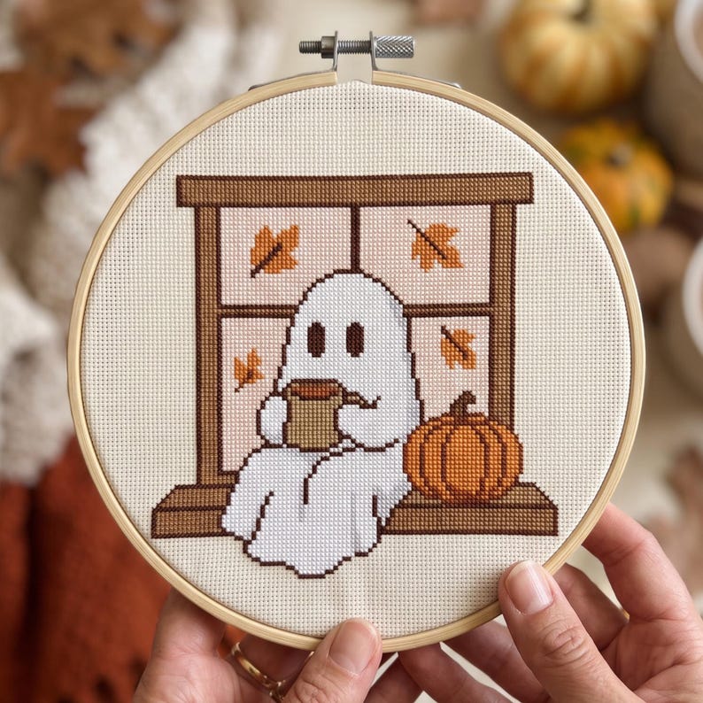 Peut inclure: Un tambour &agrave; broder circulaire en bois contenant un motif au point de croix repr&eacute;sentant un fant&ocirc;me blanc assis sur un rebord de fen&ecirc;tre marron. Le fant&ocirc;me tient une tasse marron, avec une citrouille orange &agrave; c&ocirc;t&eacute;. Des feuilles d'automne pars&egrave;ment les vitres.