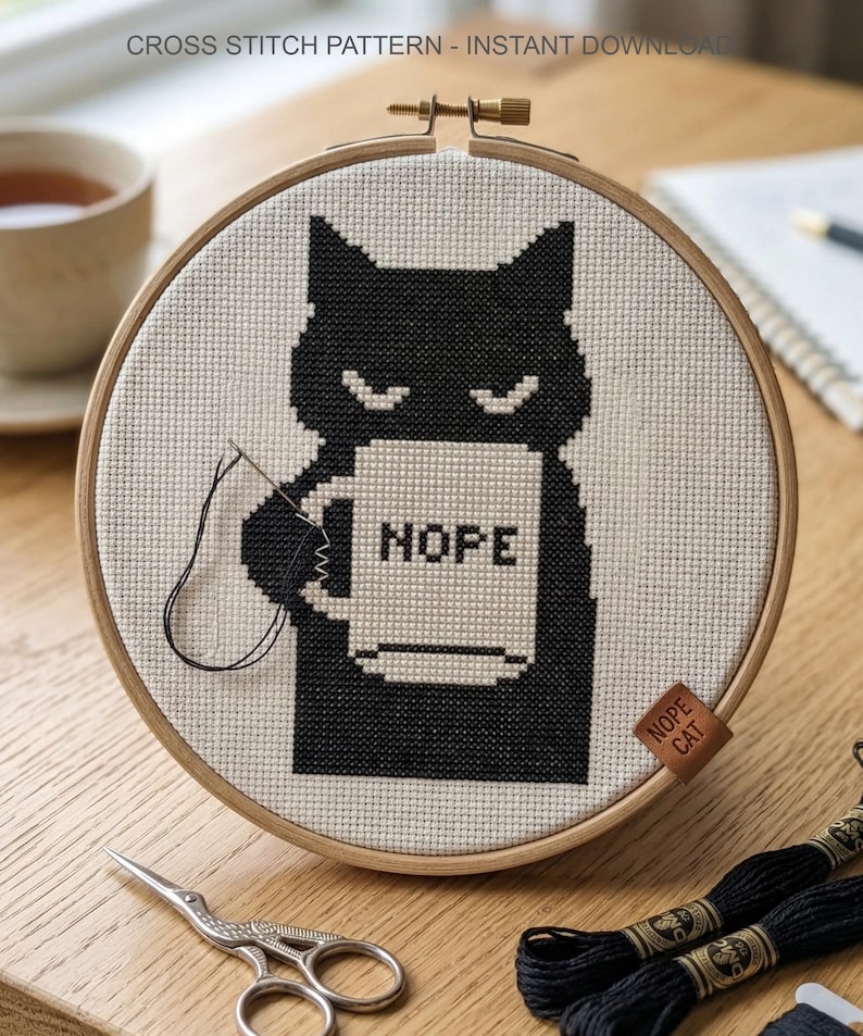 May include: A cross-stitch design of a black cat holding a mug with the word "HOPE". The cat is stitched on a beige fabric, framed in a wooden hoop. The text "CROSS STITCH PATTERN - INSTANT DOWNLOAD" is at the top.