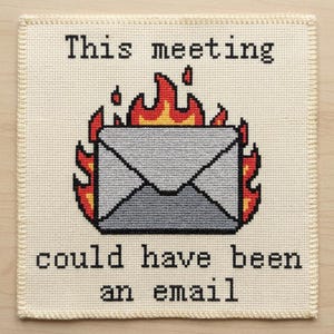 Pode incluir: Um bordado em ponto cruz quadrado sobre tecido creme apresentando um envelope cinza envolto em chamas laranjas e vermelhas. O texto preto acima do envelope diz This meeting e o texto abaixo diz could have been an email em fonte pixel.