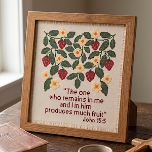 May include: A framed cross-stitch embroidery featuring a pattern of red strawberries, green leaves, and yellow flowers on cream fabric. The text reads: "The one who remains in me and I in him produces much fruit" John 15:5 in dark red lettering.