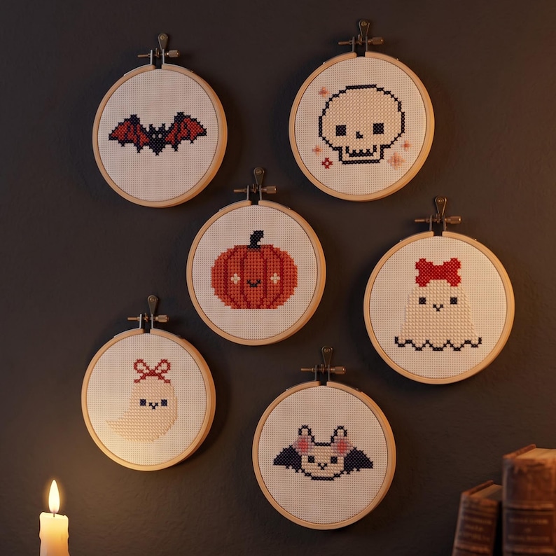 K&ouml;nnte beinhalten: Sechs runde Stickrahmen aus Holz mit wei&szlig;em Stoff und Kreuzstichmotiven. Die Designs zeigen eine schwarze Fledermaus mit roten Fl&uuml;geln, einen wei&szlig;en Totenkopf, einen orangefarbenen K&uuml;rbis sowie zwei wei&szlig;e Geister mit roten Schleifen.