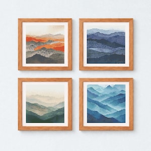 May include: Four framed art prints showcasing abstract mountain landscapes in shades of orange, blue, and green. Each print is square and set within a natural wood frame. The artwork depicts layered mountain ranges with a watercolour effect.