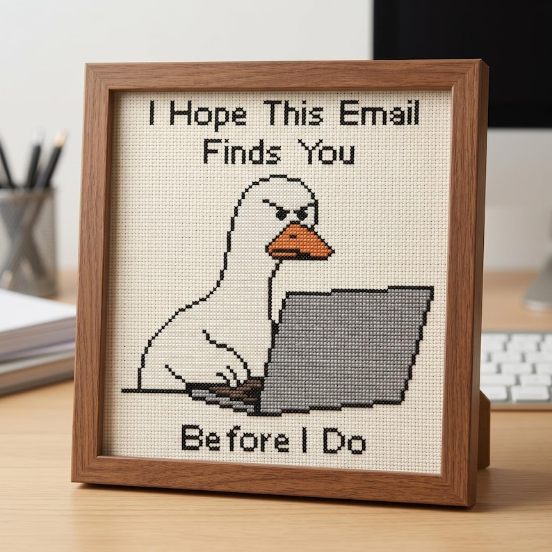 K&ouml;nnte beinhalten: Ein gerahmtes Kreuzstichbild mit einer wei&szlig;en Gans mit orangefarbenem Schnabel und w&uuml;tendem Gesichtsausdruck, die an einem grauen Laptop tippt. Der Text "I Hope This Email Finds You BEFORE I Do" ist in schwarzem Garn auf cremefarbenem Stoff gestickt.